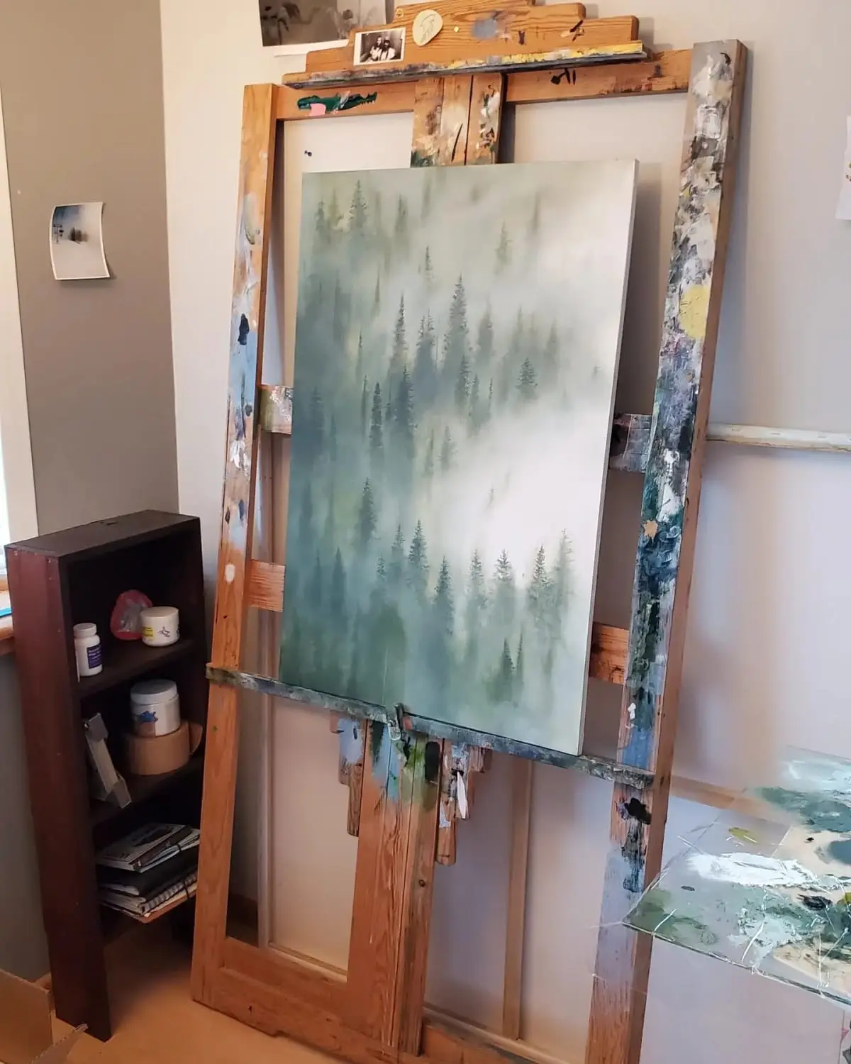 Misty evergreen forest painting on an easel in Branda Avis’s studio