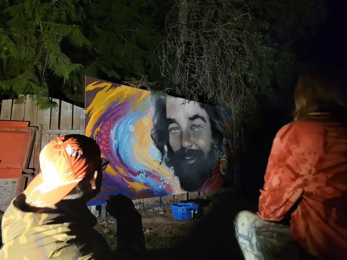 A finished live-painted portrait lit at night, with two onlookers watching from the foreground