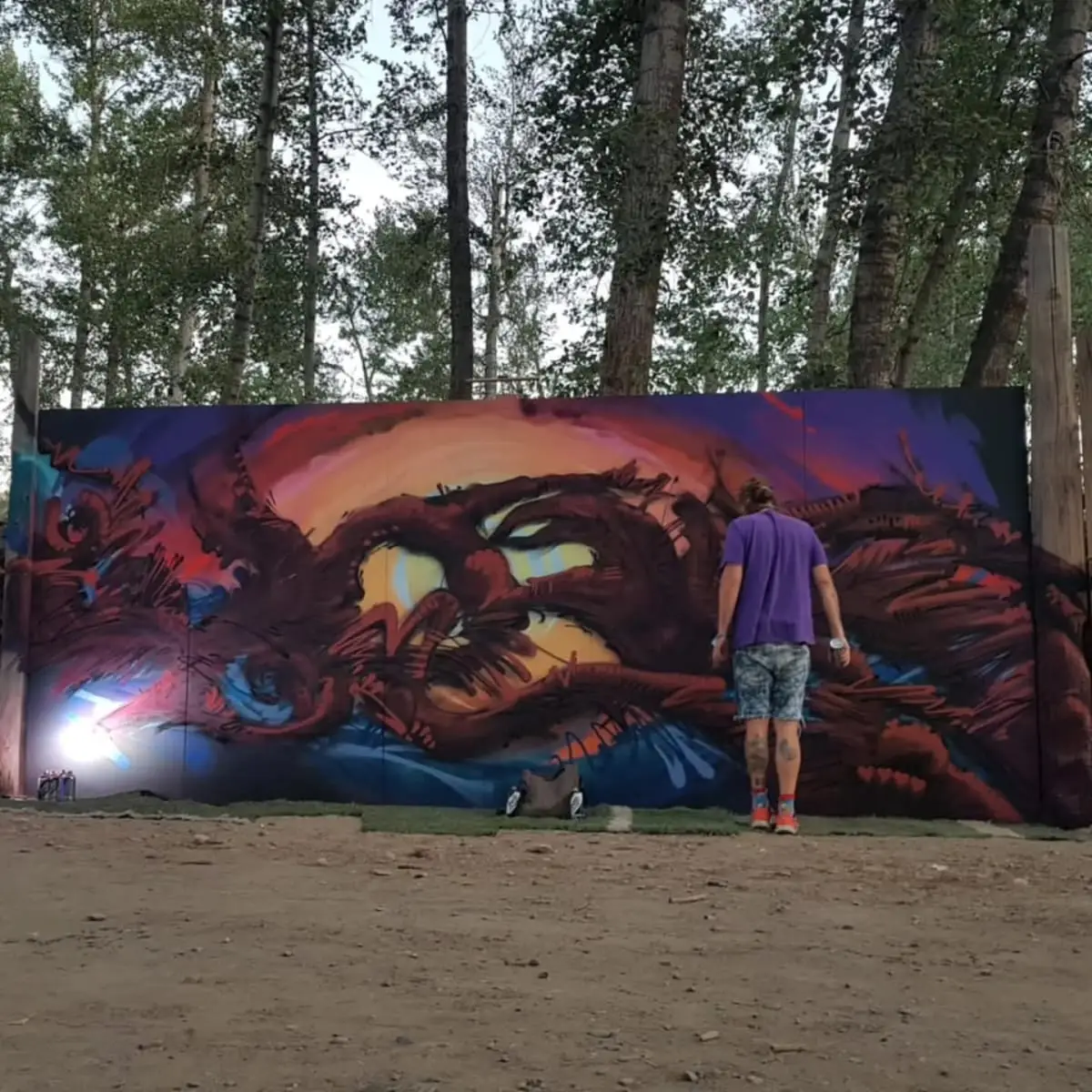 Andreas Tiedemann painting a large red and orange organic mural on a wall set among cottonwood trees