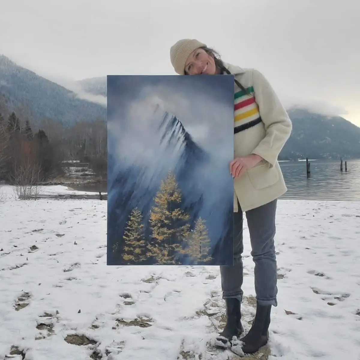 Branda Avis holding a mountain and evergreen tree painting outdoors in the snow