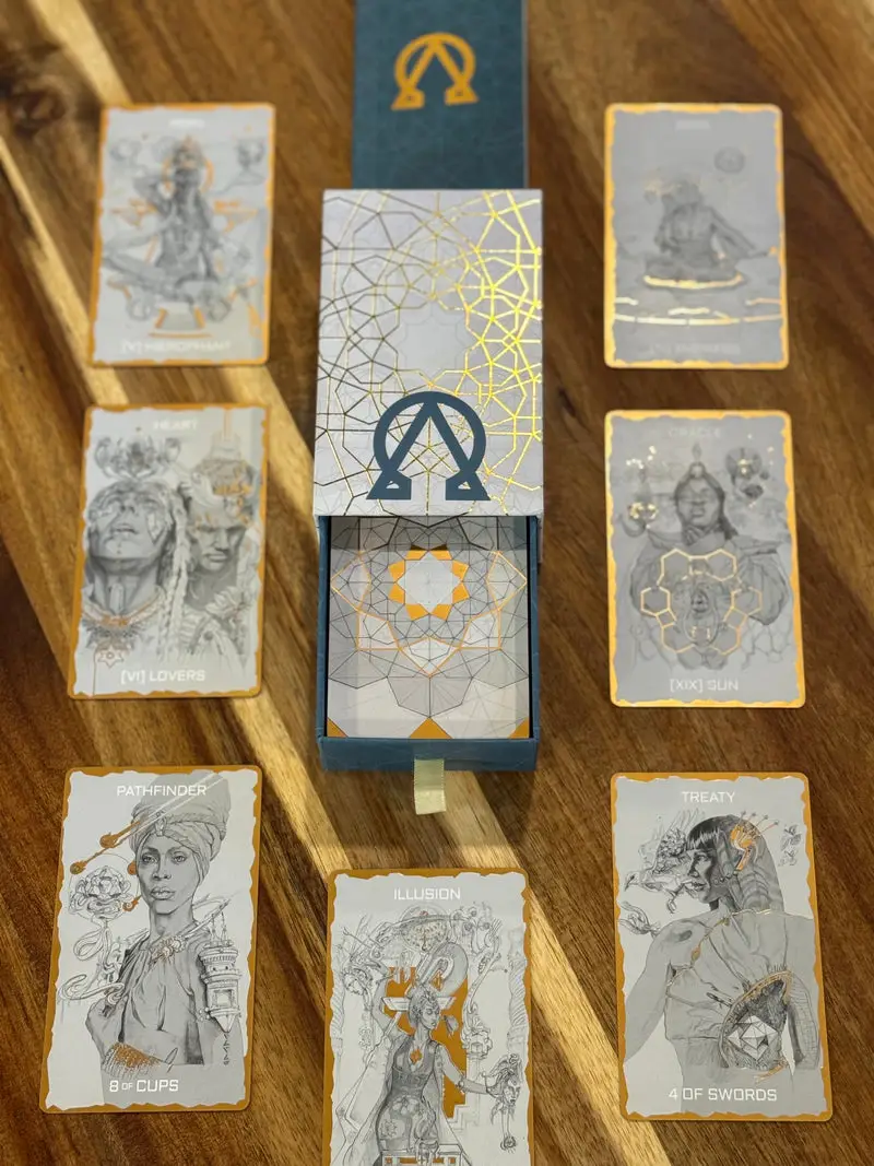 Tarot One’s open presentation box surrounded by illustrated cards with gold metallic details on a wooden table